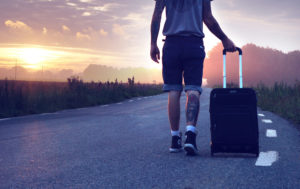 スーツケースを引きながら道路を歩く旅人